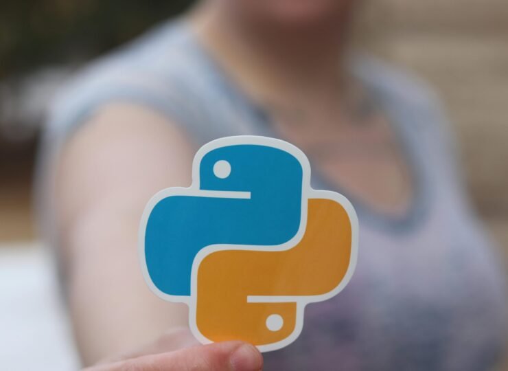 Person holding Python logo sticker with blurred background, highlighting programming focus.