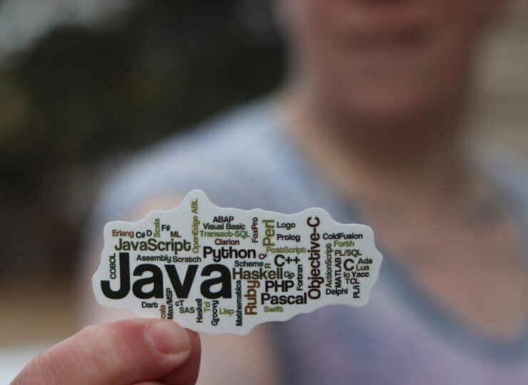 Close-up of a person holding a sticker with various programming languages listed on it.